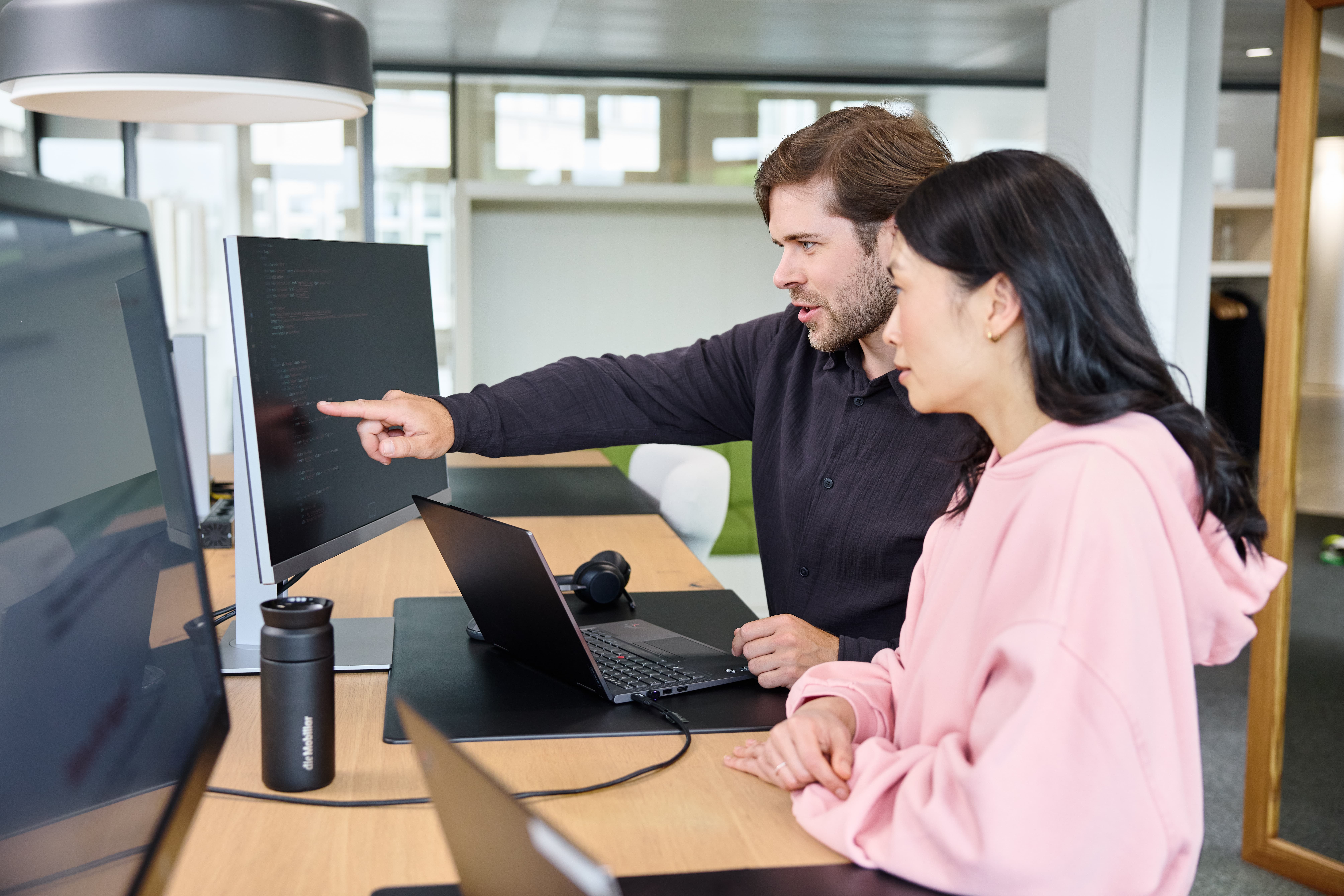 Deux hommes sont en réunion, assis dans des fauteuils rouges, l’un d’eux a un ordinateur portable.